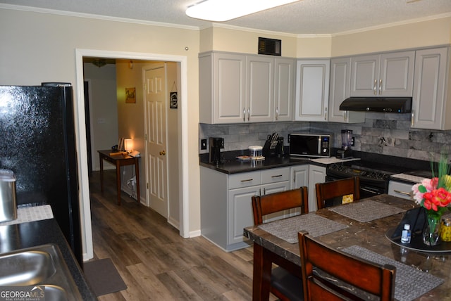 kitchen featuring tasteful backsplash, wood finished floors, ornamental molding, black appliances, and under cabinet range hood