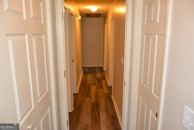 hallway featuring visible vents, attic access, and dark wood-type flooring