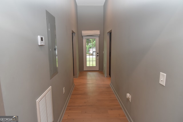 hallway with electric panel, a towering ceiling, visible vents, baseboards, and light wood-style floors