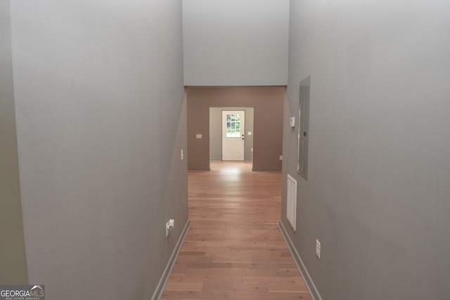 corridor with light wood finished floors, electric panel, visible vents, and a high ceiling