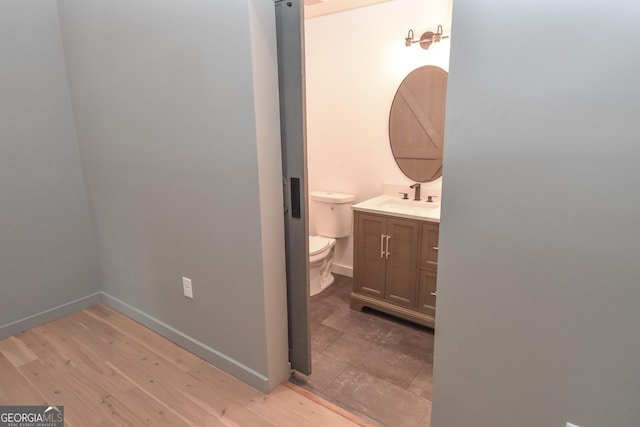 half bath featuring vanity, toilet, baseboards, and wood finished floors