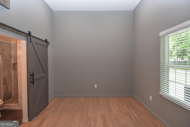 unfurnished room featuring a barn door, light wood-type flooring, and baseboards