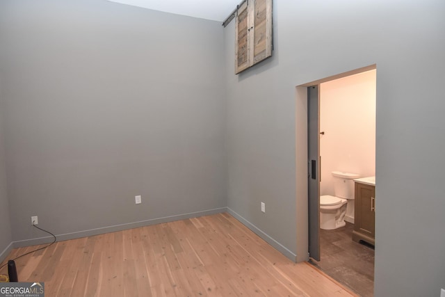 unfurnished bedroom with ensuite bathroom, baseboards, and light wood-style floors