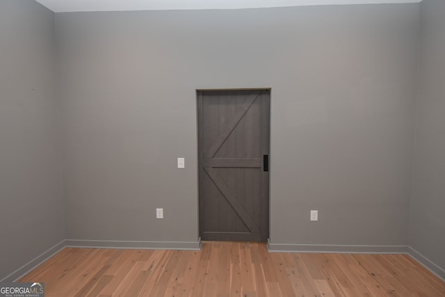 unfurnished room with baseboards, light wood-style flooring, and a barn door