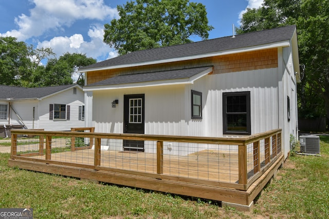 back of property with central AC unit, a wooden deck, a shingled roof, and a lawn
