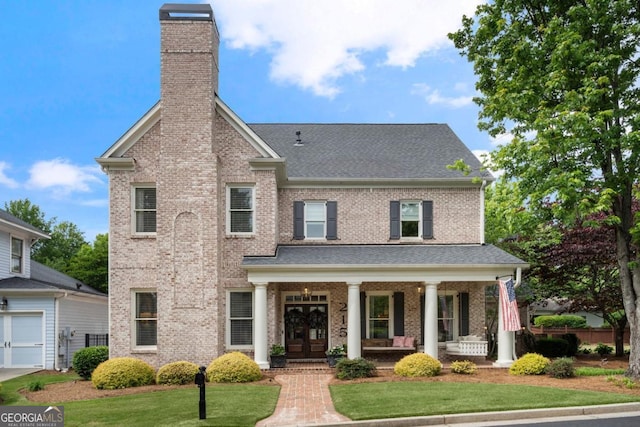 traditional-style home with a chimney, a front lawn, a shingled roof, a porch, and brick siding
