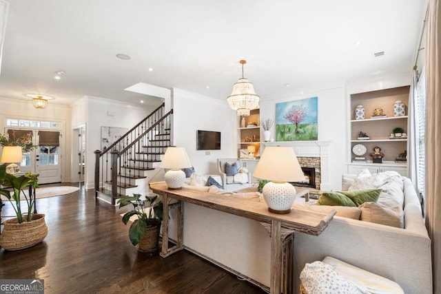 living room featuring built in features, stairs, crown molding, a fireplace, and dark wood-style floors