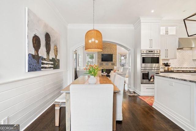 dining space featuring ornamental molding, arched walkways, and dark wood-type flooring