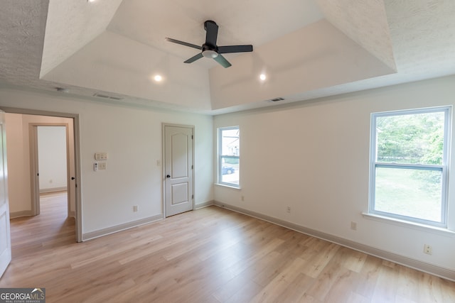 unfurnished bedroom featuring a tray ceiling, light wood-type flooring, visible vents, baseboards, and ceiling fan