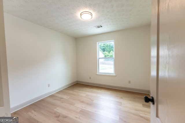empty room with light wood-style floors, visible vents, baseboards, and a textured ceiling