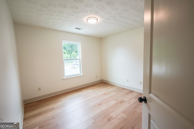 empty room featuring light wood-type flooring, baseboards, visible vents, and a textured ceiling