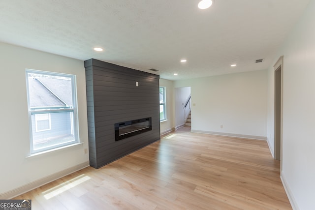 unfurnished living room featuring stairs, light wood finished floors, and a large fireplace