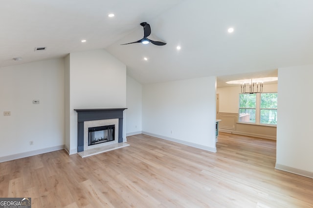 unfurnished living room with vaulted ceiling, a ceiling fan, a fireplace with raised hearth, and light wood-style floors
