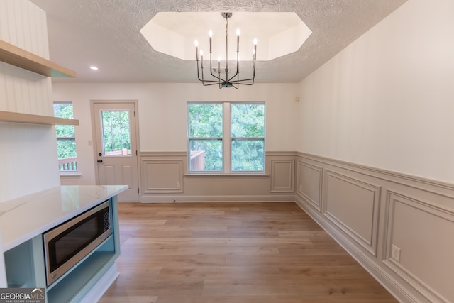 unfurnished dining area with light wood-style flooring, recessed lighting, a textured ceiling, a chandelier, and a wainscoted wall