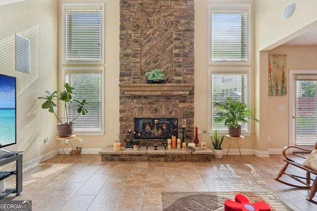 living area with a towering ceiling, baseboards, a stone fireplace, and tile patterned floors
