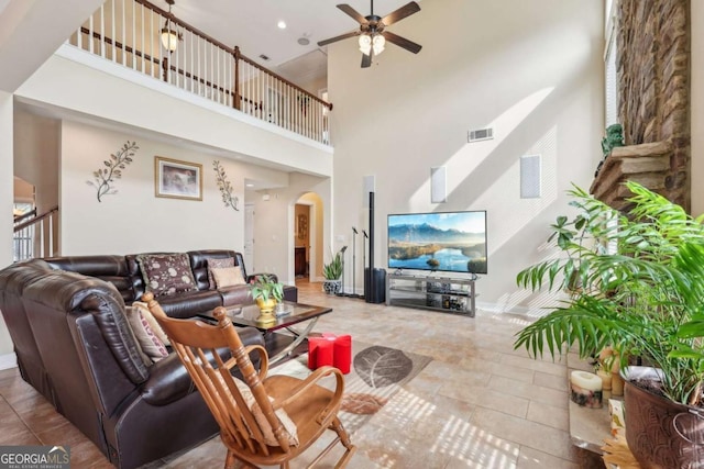 living area with a ceiling fan, a high ceiling, visible vents, baseboards, and arched walkways