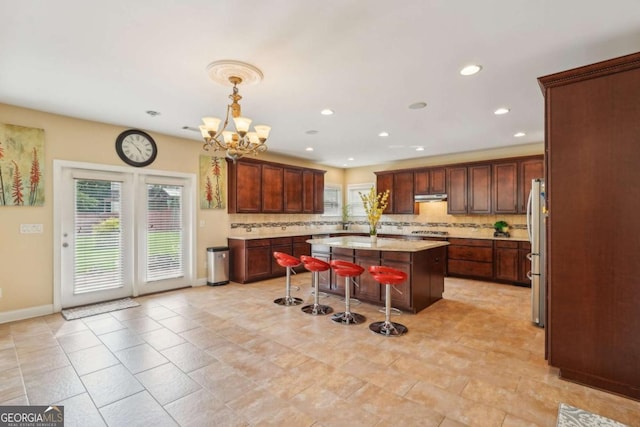 kitchen with freestanding refrigerator, under cabinet range hood, a breakfast bar, decorative backsplash, and a kitchen island