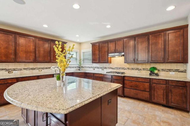 kitchen with light stone counters, decorative backsplash, and under cabinet range hood
