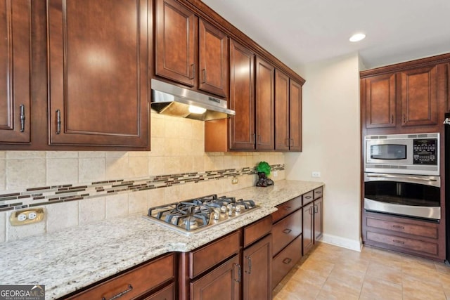 kitchen with under cabinet range hood, stainless steel appliances, backsplash, and light stone counters
