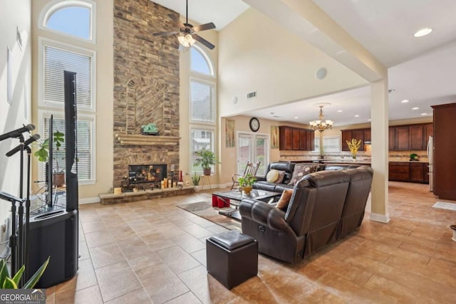 living area featuring baseboards, a stone fireplace, visible vents, ceiling fan with notable chandelier, and a high ceiling