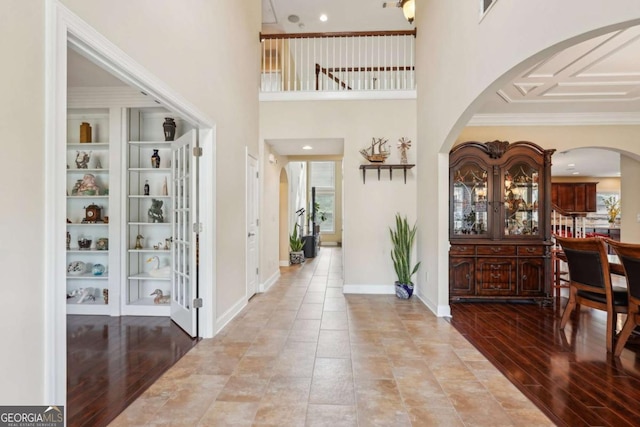 foyer featuring wood finished floors, a high ceiling, visible vents, arched walkways, and ornamental molding