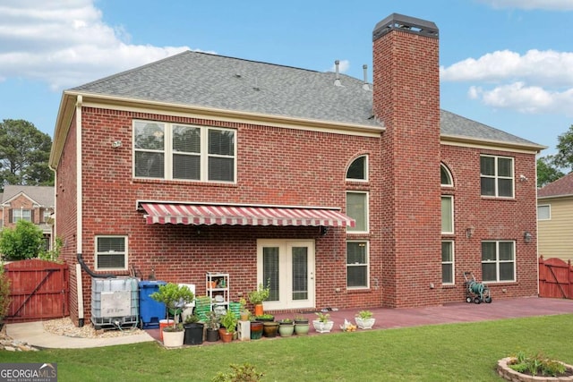 back of property with a gate, a chimney, a lawn, brick siding, and a patio area