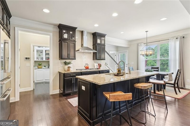kitchen with stainless steel gas stovetop, glass insert cabinets, light stone counters, a sink, and wall chimney range hood