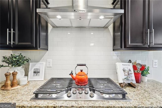 kitchen featuring light stone countertops, decorative backsplash, wall chimney exhaust hood, and stainless steel gas cooktop