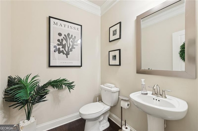 half bathroom with baseboards, toilet, a sink, crown molding, and wood finished floors