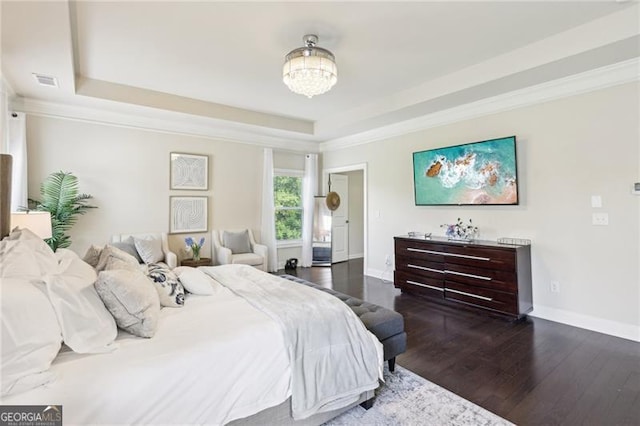 bedroom featuring baseboards, wood finished floors, a raised ceiling, and visible vents