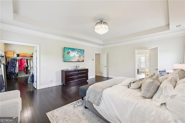 bedroom with a closet, ornamental molding, wood-type flooring, a raised ceiling, and a spacious closet