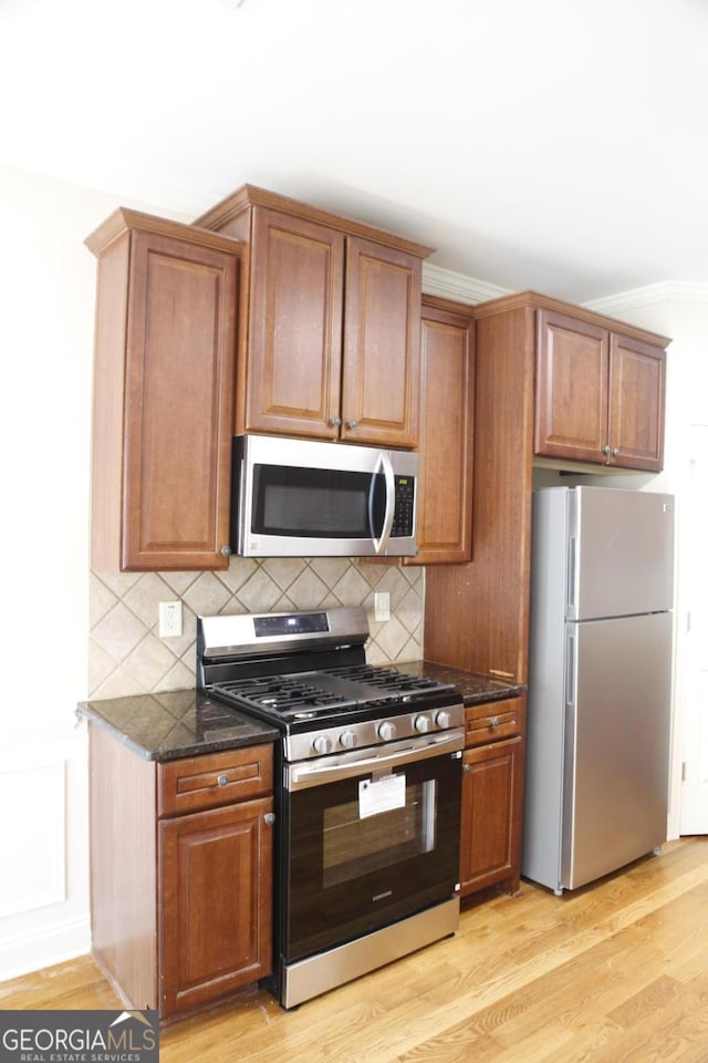 kitchen featuring dark stone counters, stainless steel appliances, crown molding, light wood-type flooring, and tasteful backsplash