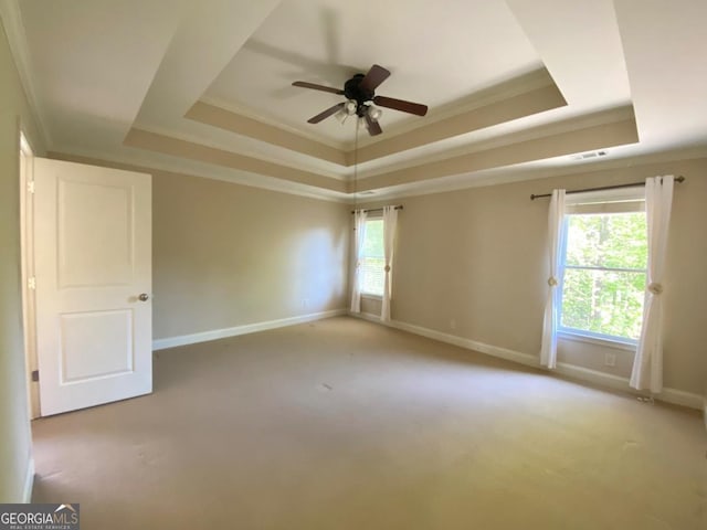 empty room with light colored carpet, ornamental molding, a ceiling fan, a raised ceiling, and baseboards