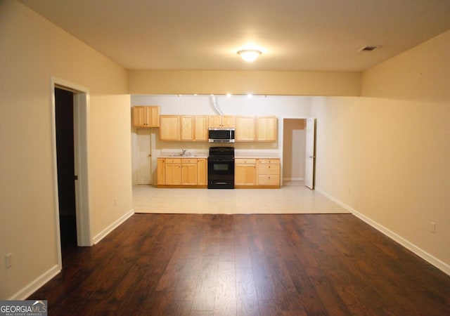 kitchen featuring stainless steel microwave, a sink, wood finished floors, light brown cabinetry, and stove