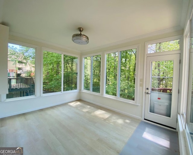 unfurnished sunroom featuring ornamental molding, plenty of natural light, baseboards, and wood finished floors