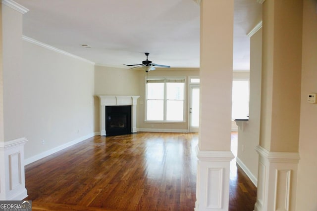 unfurnished living room with wood finished floors, a ceiling fan, ornate columns, baseboards, and a glass covered fireplace