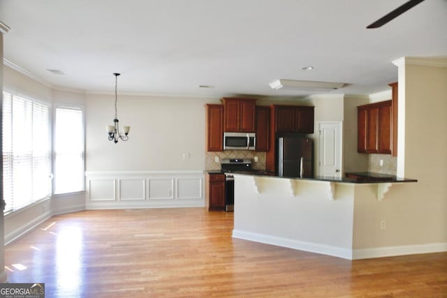 kitchen with a peninsula, light wood-style flooring, a kitchen bar, stainless steel appliances, and ornamental molding