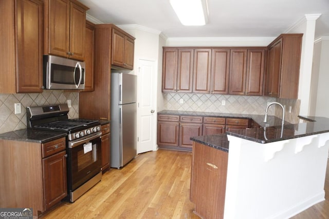 kitchen featuring a peninsula, dark stone counters, light wood-type flooring, appliances with stainless steel finishes, and ornamental molding