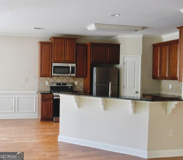 kitchen with crown molding, a kitchen bar, dark countertops, and appliances with stainless steel finishes