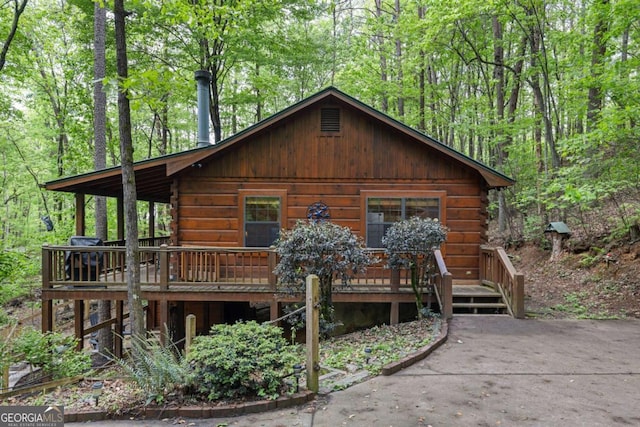 exterior space featuring a wooded view, a wooden deck, and log exterior