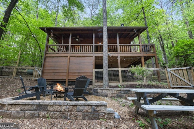 rear view of property featuring a ceiling fan, a wooden deck, a fire pit, and fence