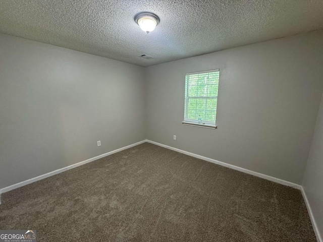 empty room featuring a textured ceiling, visible vents, baseboards, and dark carpet