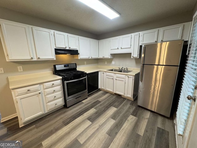 kitchen with under cabinet range hood, white cabinets, dark wood-type flooring, and appliances with stainless steel finishes