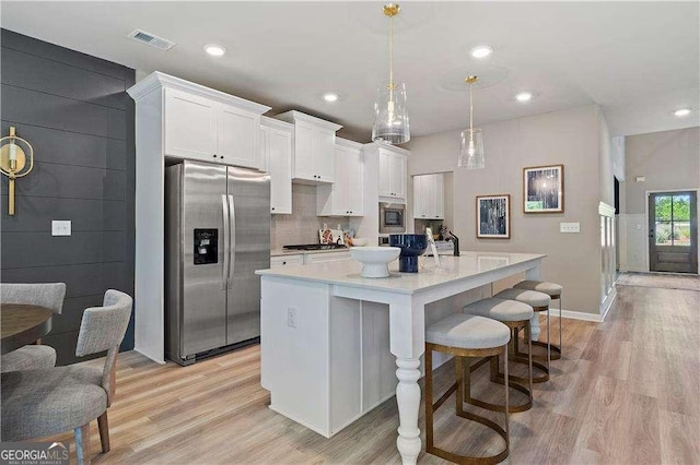 kitchen featuring light wood finished floors, an island with sink, stainless steel appliances, white cabinets, and visible vents