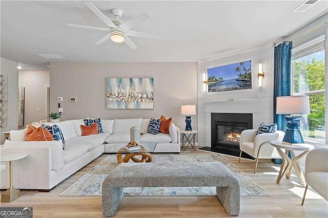 living area featuring a large fireplace, visible vents, wood finished floors, and ceiling fan
