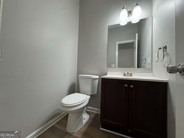 half bath featuring baseboards, vanity, toilet, and wood finished floors