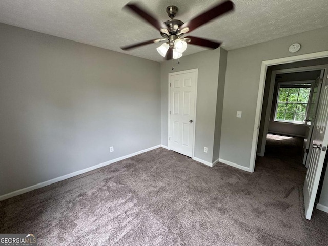 unfurnished bedroom with ceiling fan, a textured ceiling, baseboards, and dark carpet