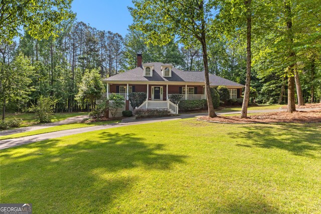 view of front of property featuring a front lawn, a porch, a chimney, and aphalt driveway