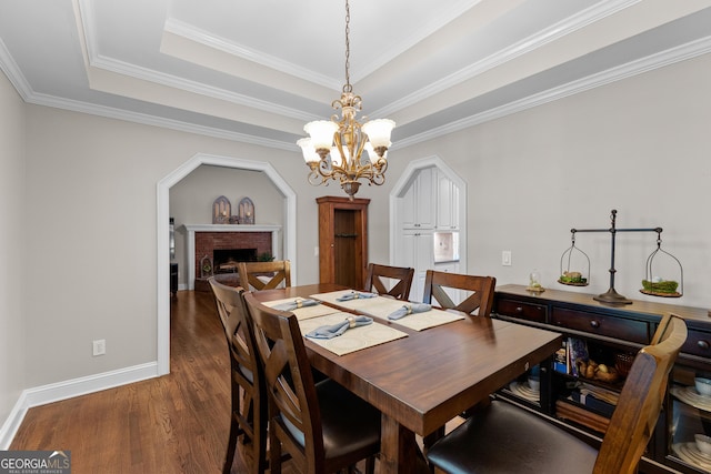 dining room with an inviting chandelier, a tray ceiling, a fireplace, dark wood finished floors, and ornamental molding