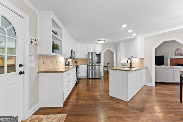 kitchen with a peninsula, a sink, stainless steel appliances, white cabinets, and decorative backsplash